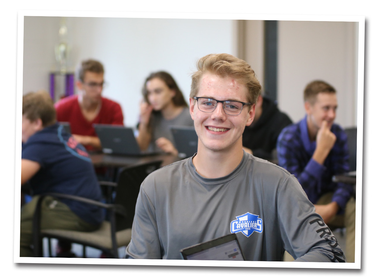 A teenage student poses for a picture at his desk.