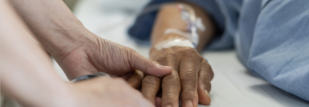 Person holding dying person's hand in hospital