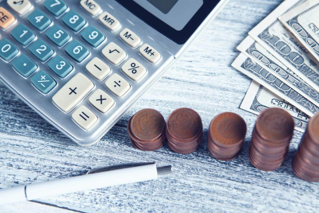 Calculator, pen, pennies, and dollars on a desk.
