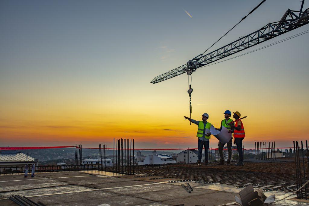 Construction crew high up on a building and dusk with a crane in the background.